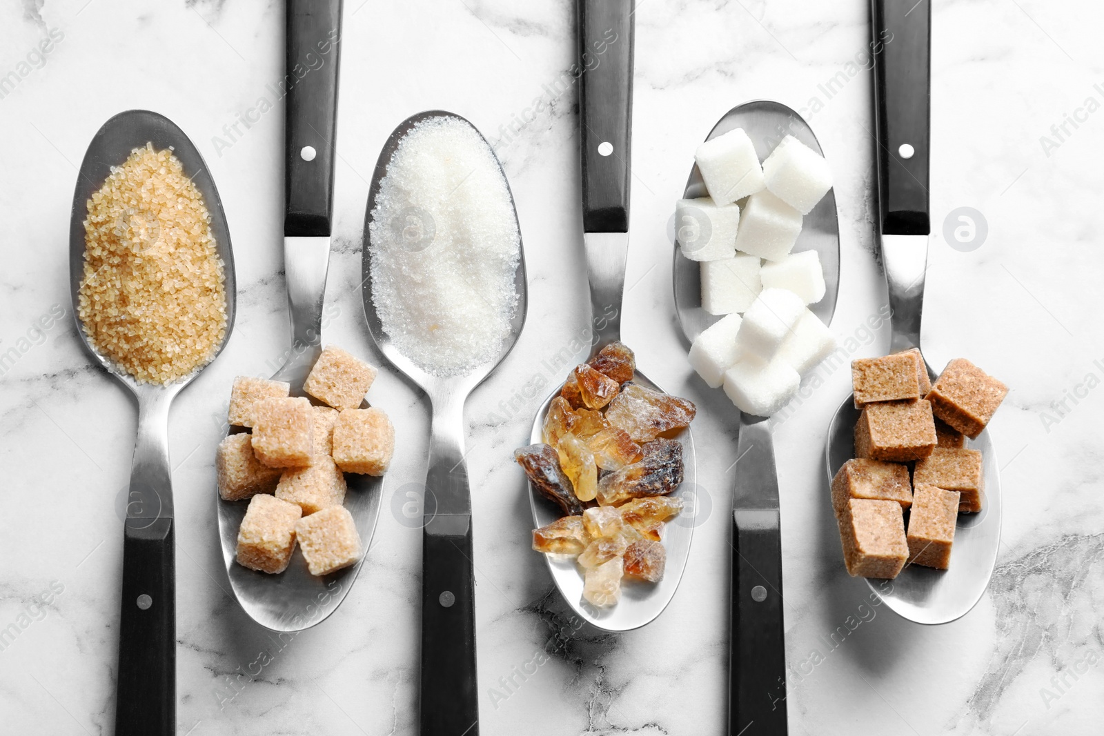 Photo of Spoons with different types of sugar on marble background