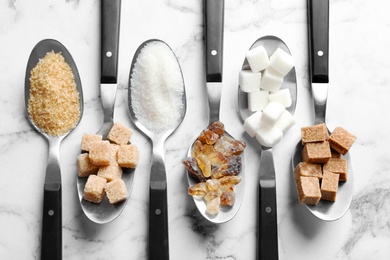 Photo of Spoons with different types of sugar on marble background