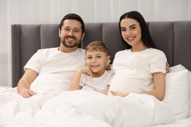 Photo of Portrait of happy pregnant woman with her son and husband in bed at home