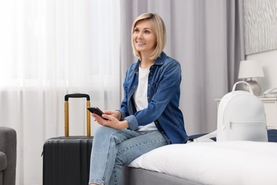 Smiling guest with smartphone relaxing on bed in stylish hotel room