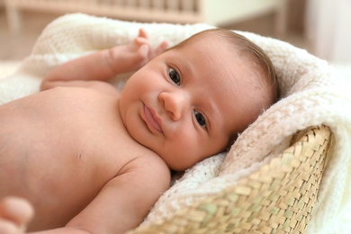 Photo of Cute little baby lying on knitted plaid in cradle
