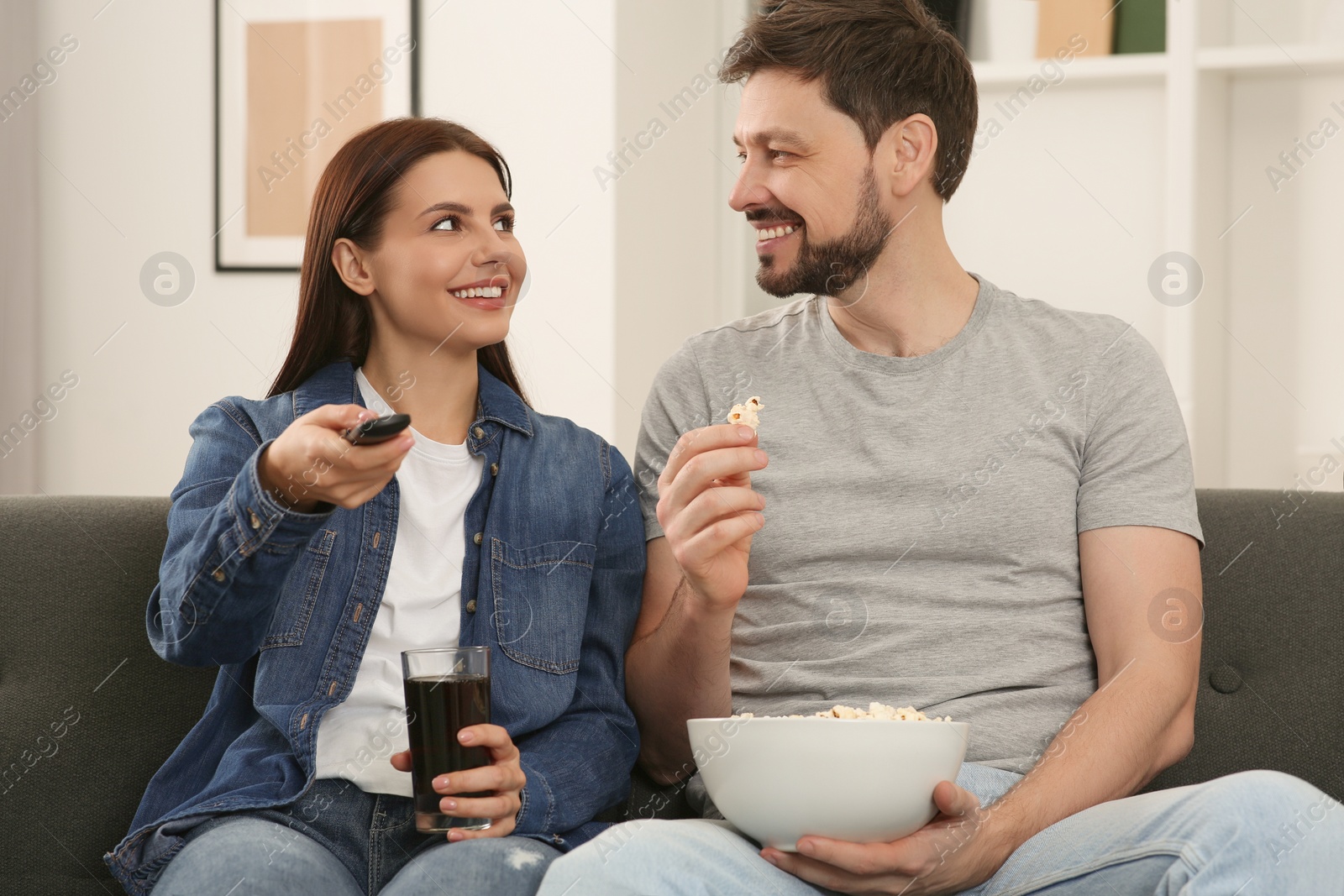 Photo of Happy couple watching show at home. Woman changing TV channels with remote control