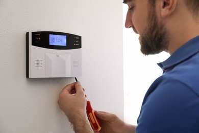 Photo of Man installing home security system on white wall in room, closeup