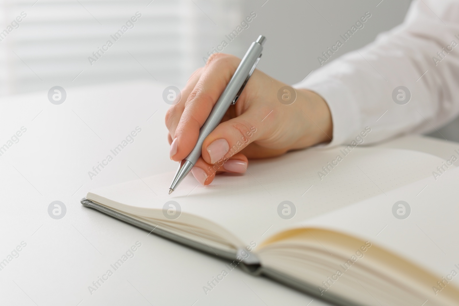 Photo of Woman writing in notebook at white table, closeup