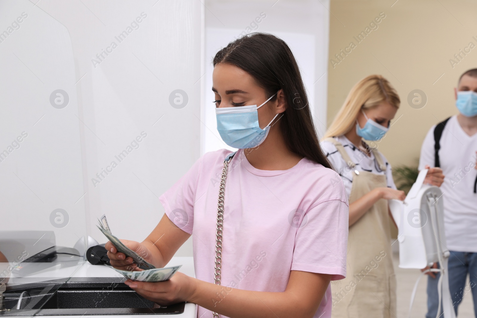 Photo of Woman with protective mask counting money at cash department window in bank. Currency exchange