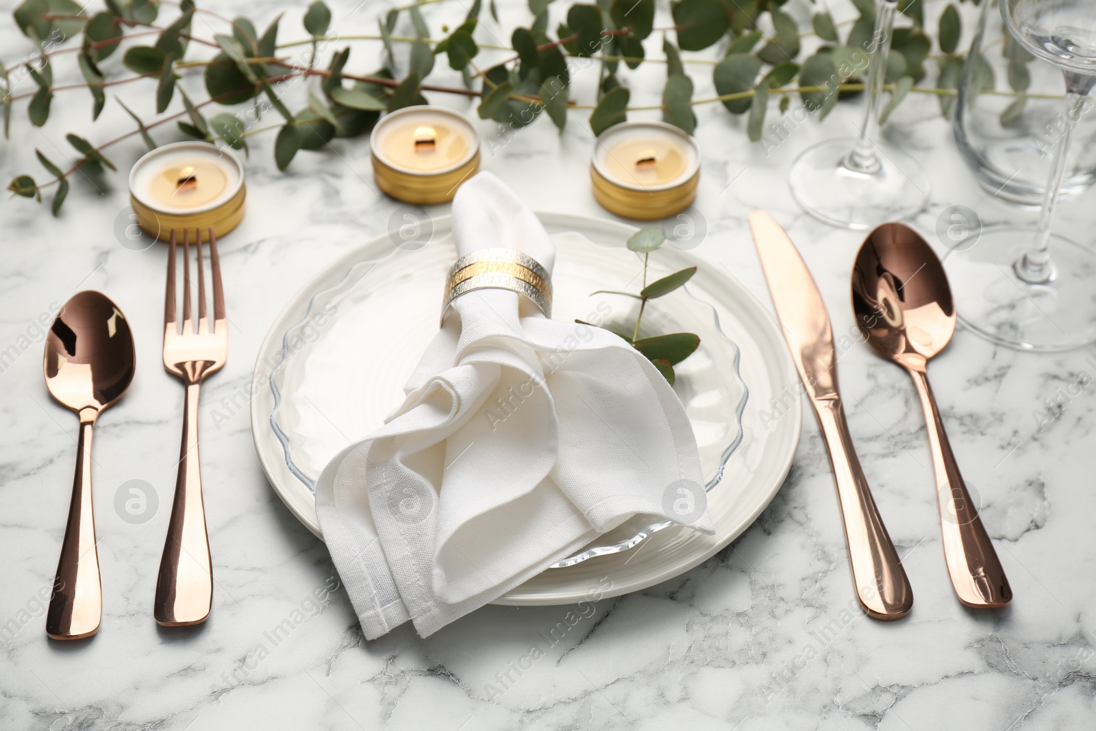 Photo of Beautiful place setting with candles and eucalyptus on white marble table