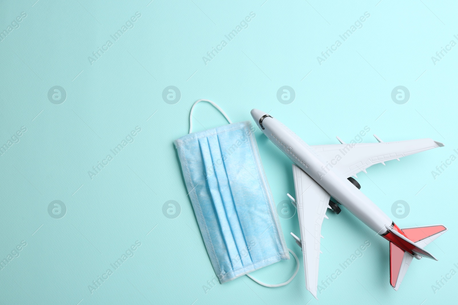 Photo of Toy airplane and protective mask on light blue background, flat lay with space for text. Travelling during coronavirus pandemic