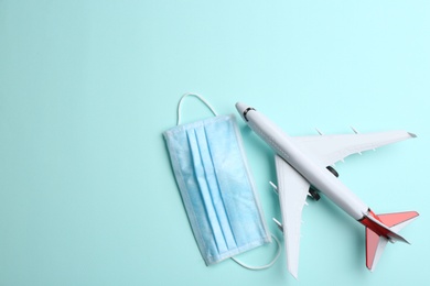 Photo of Toy airplane and protective mask on light blue background, flat lay with space for text. Travelling during coronavirus pandemic