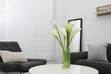 Photo of Beautiful calla lily flowers in glass vase on white table at home