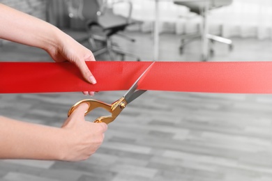 Woman cutting red ribbon on blurred background