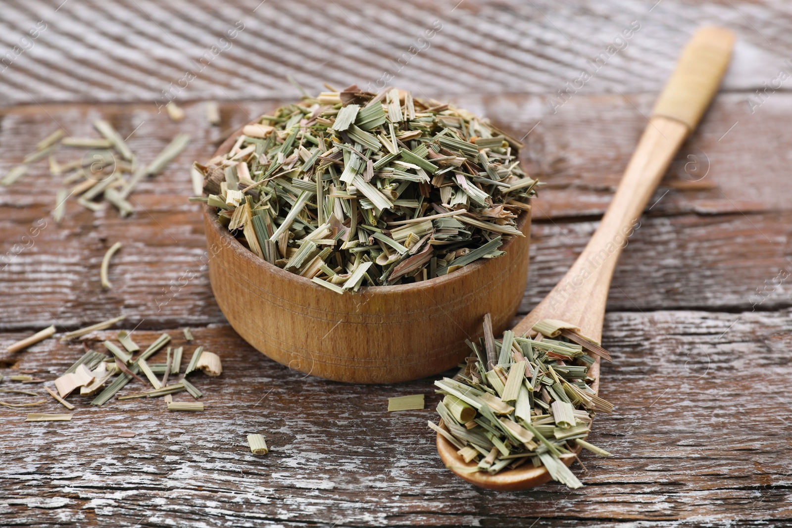 Photo of Bowl and spoon of aromatic dried lemongrass on wooden table