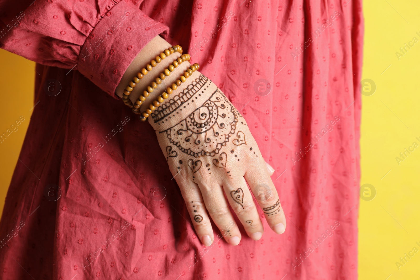 Photo of Woman with beautiful henna tattoo on hand against yellow background, closeup. Traditional mehndi