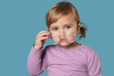 Photo of Cute little girl with glasses on light blue background
