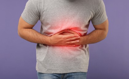 Man suffering from stomach pain on purple background, closeup