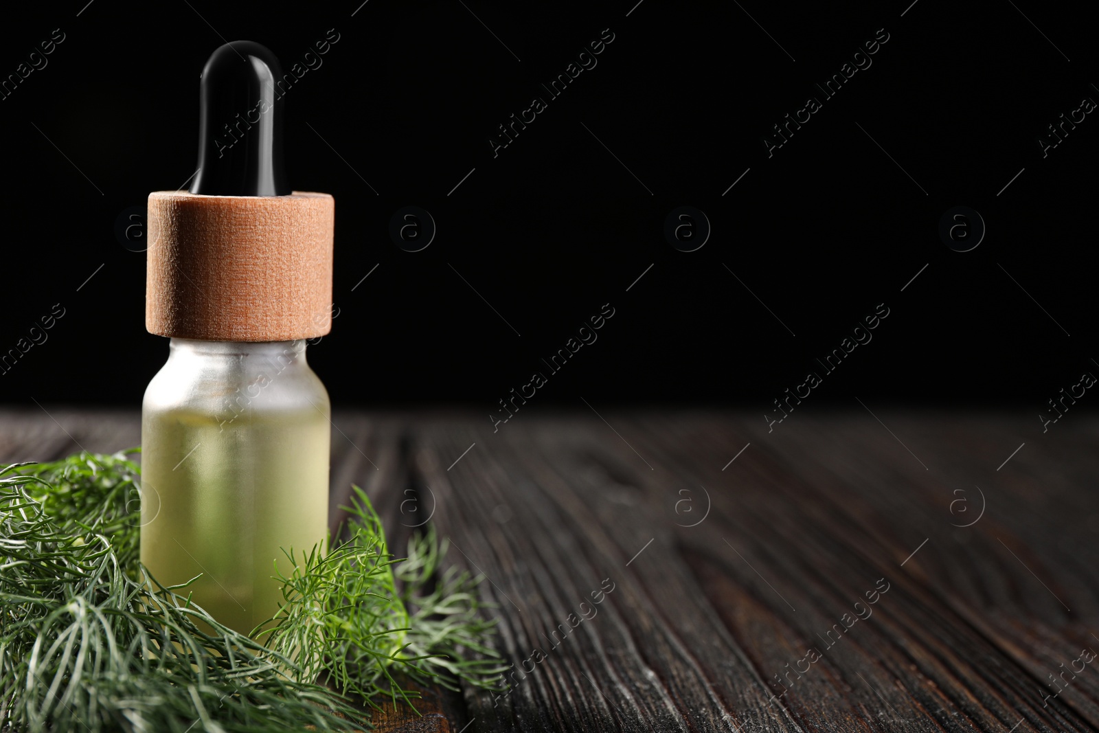 Photo of Bottle of essential oil and fresh dill on wooden table, closeup. Space for text