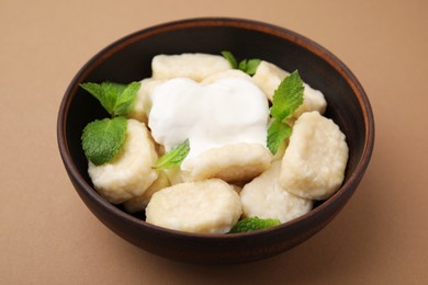 Photo of Bowl of tasty lazy dumplings with sour cream and mint leaves on light brown background