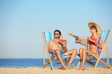 Photo of Young couple with watermelon slices in beach chairs at seacoast. Space for text