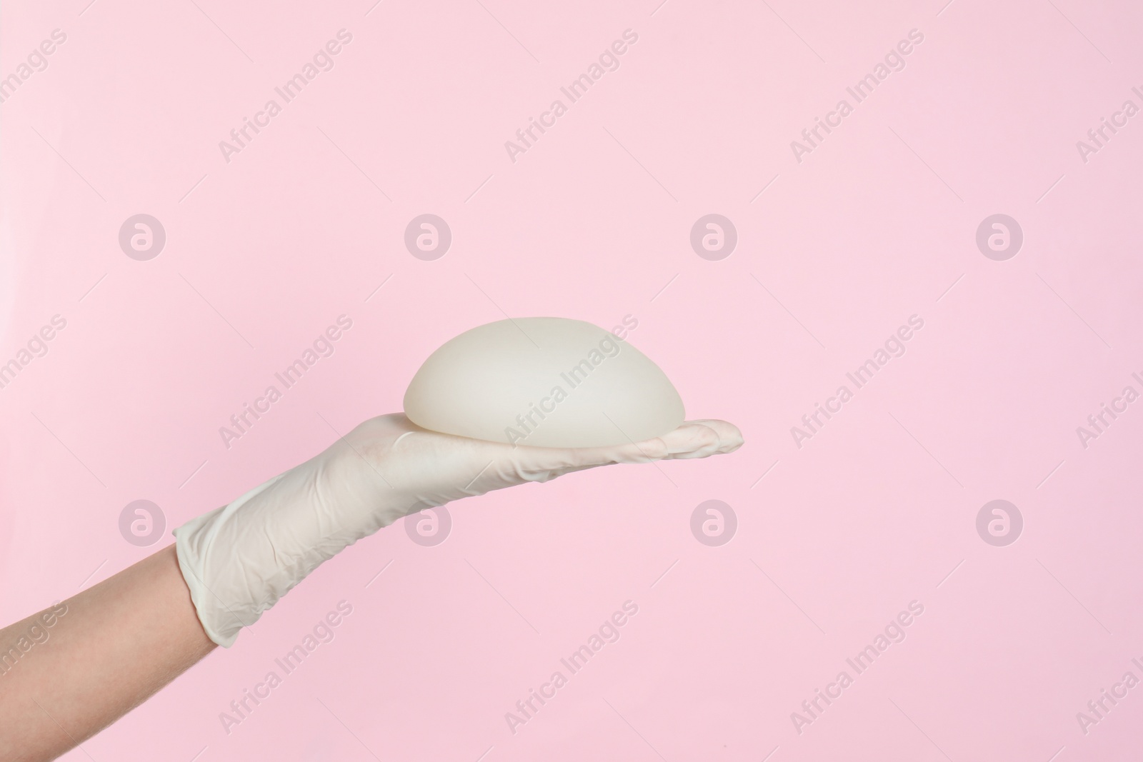 Photo of Doctor holding silicone implant for breast augmentation on color background, space for text. Cosmetic surgery