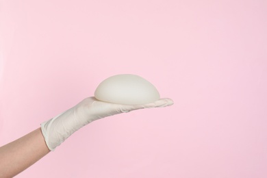 Photo of Doctor holding silicone implant for breast augmentation on color background, space for text. Cosmetic surgery