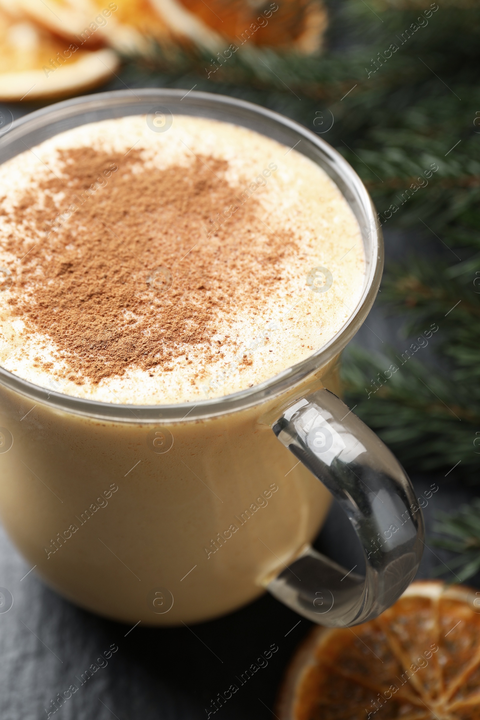 Photo of Glass cup of delicious eggnog with cinnamon on gray table, closeup