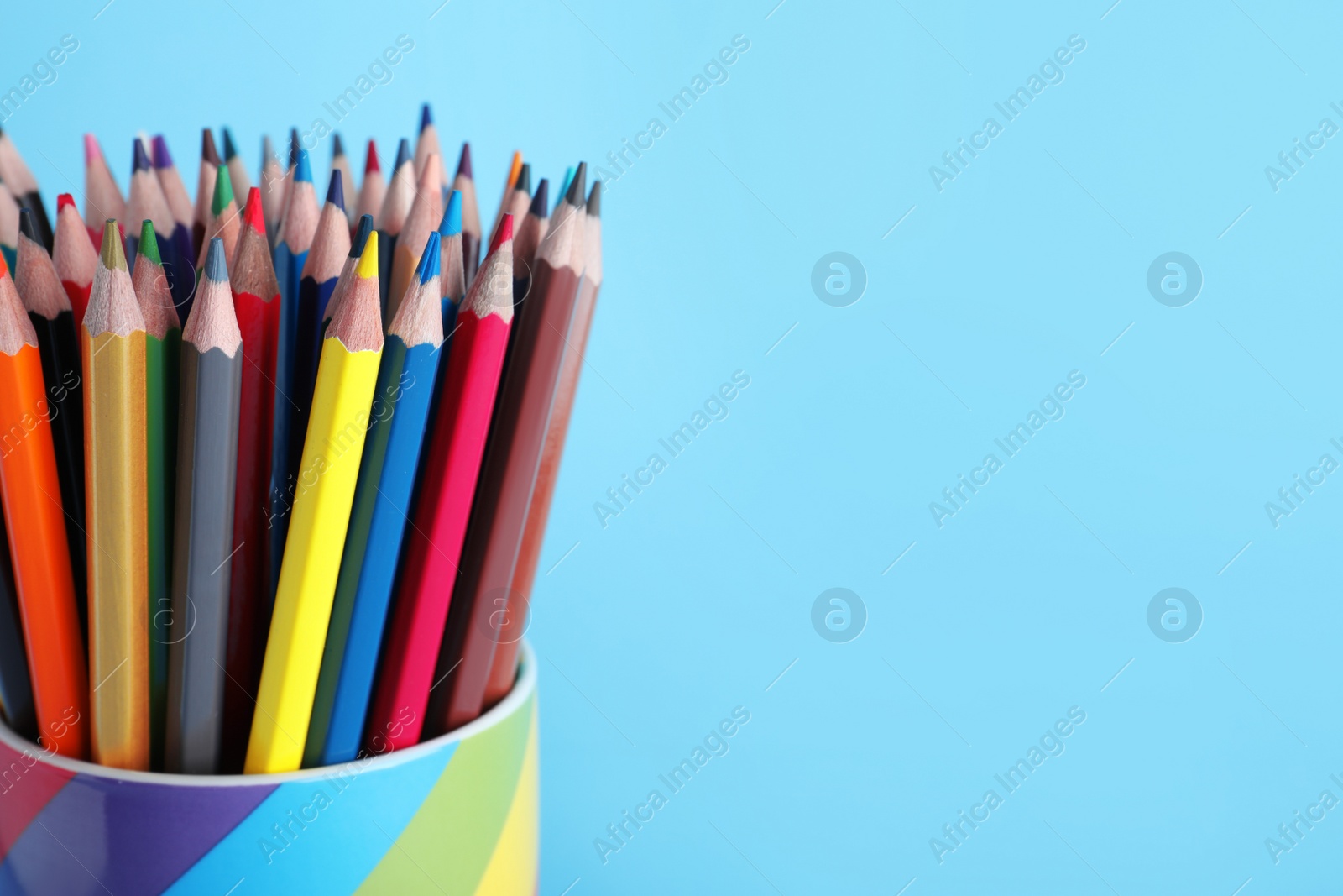 Photo of Colorful pencils in cup on light blue background, closeup. Space for text
