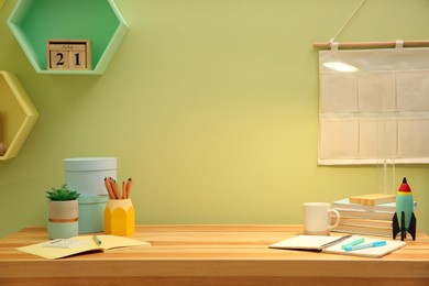 Photo of Stylish workplace with stationery on wooden desk near light green wall. Interior design