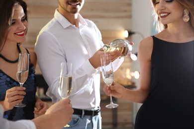 Photo of Man pouring champagne into glasses at party indoors, closeup