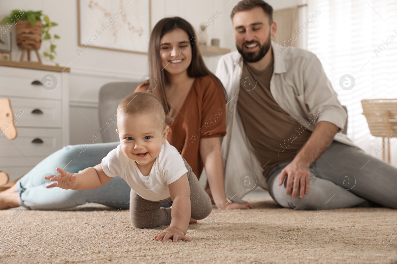 Photo of Happy parents watching their baby crawl on floor at home