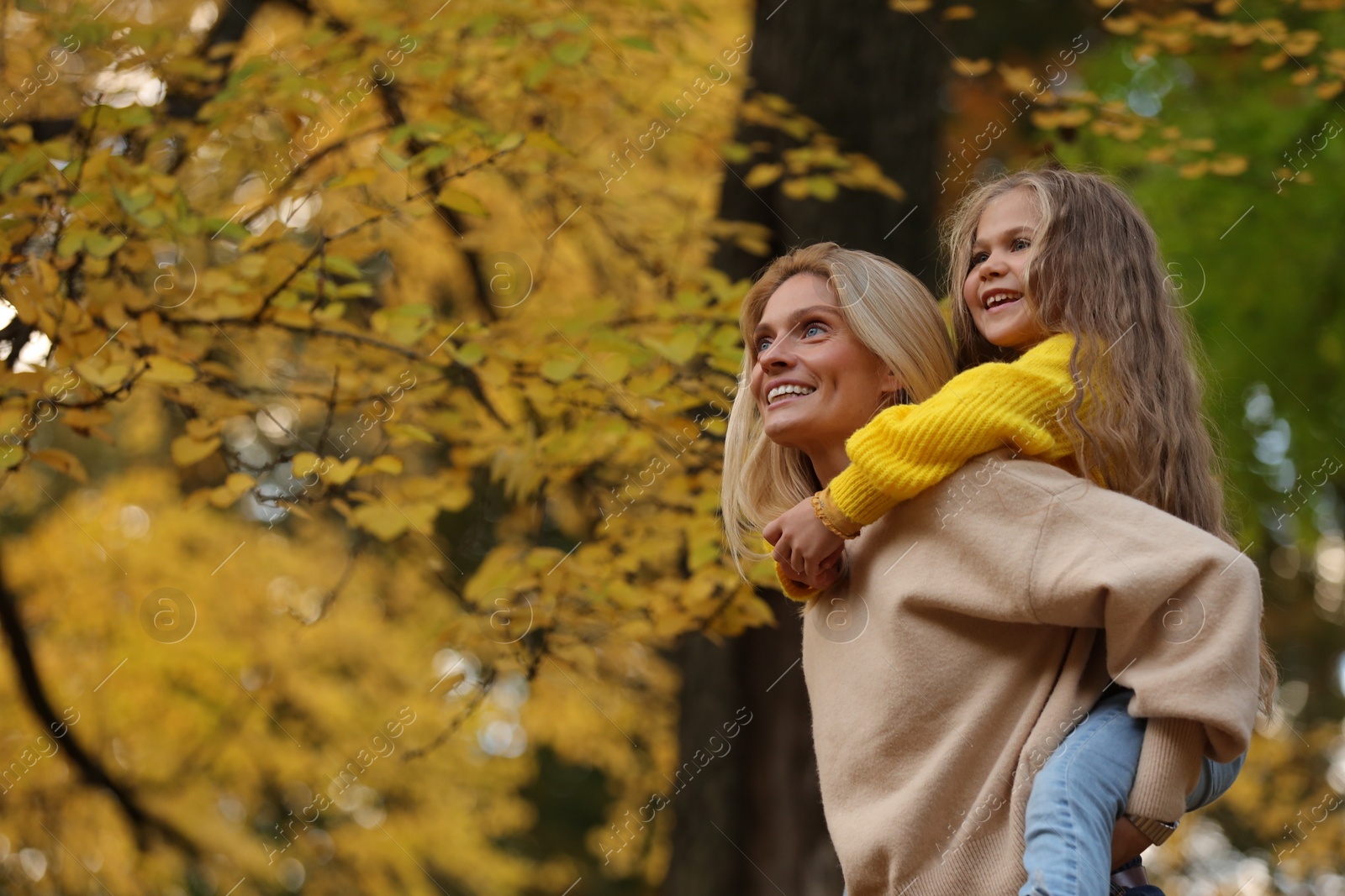 Photo of Portrait of happy mother and daughter in autumn park. Space for text