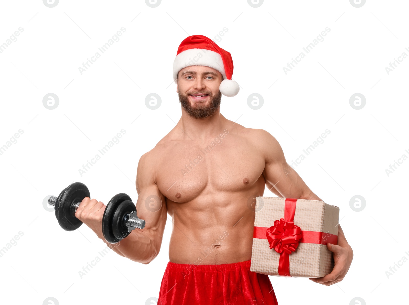 Photo of Attractive young man with muscular body in Santa hat holding Christmas gift box and dumbbell on white background