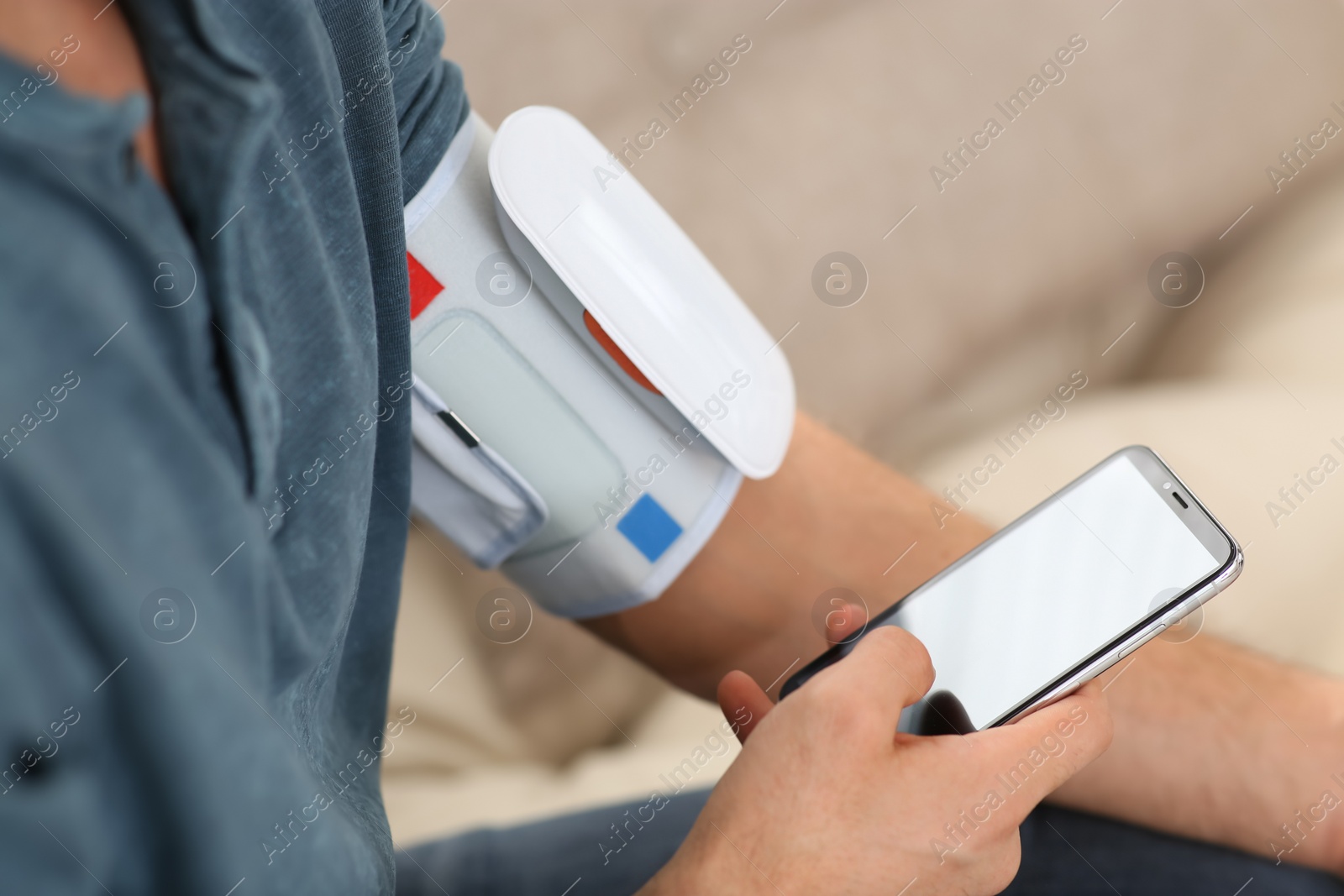 Photo of Man checking blood pressure with modern monitor and smartphone indoors, closeup