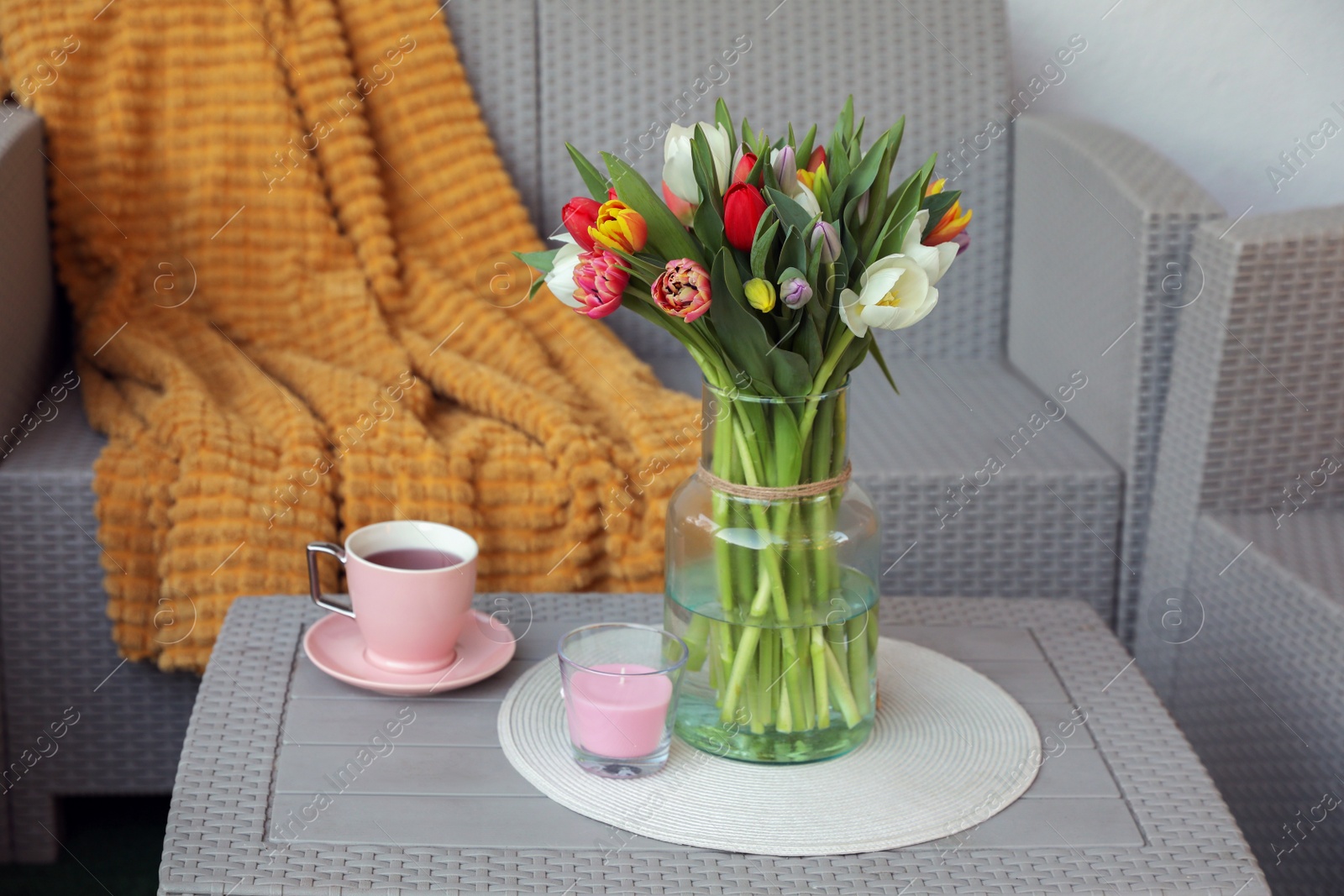 Photo of Beautiful bouquet of colorful tulips and cup with drink on rattan garden table