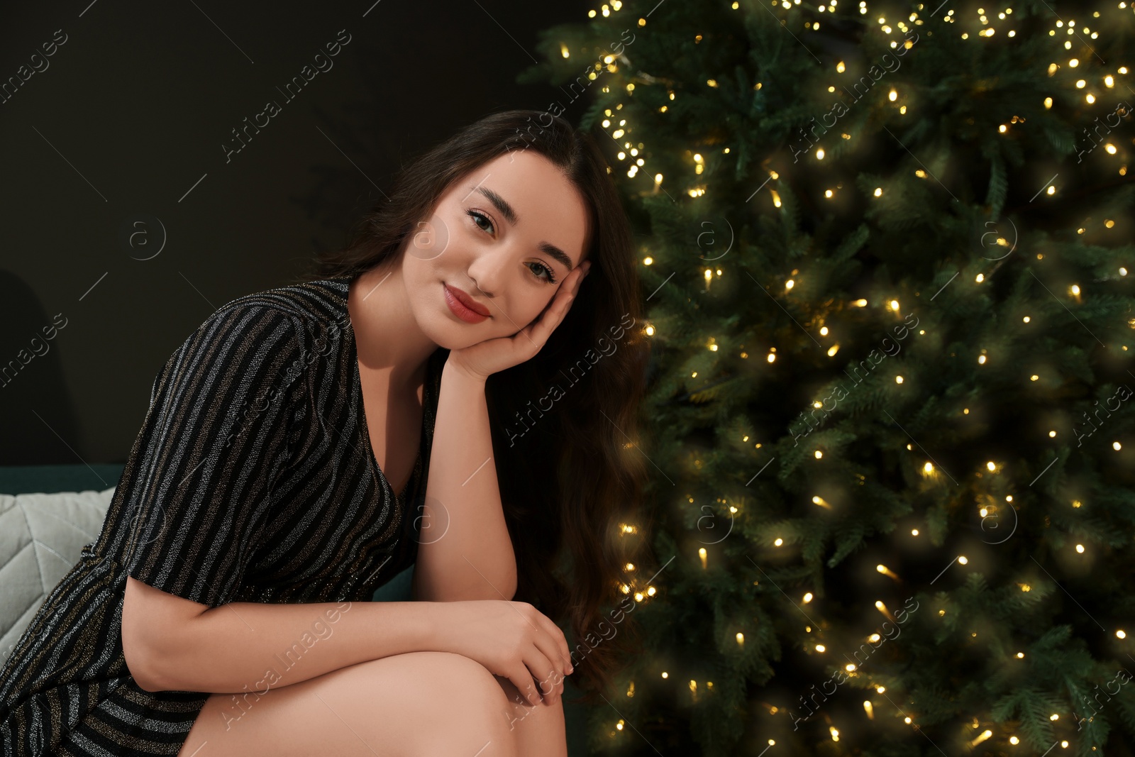 Photo of Beautiful woman near Christmas tree with golden lights indoors