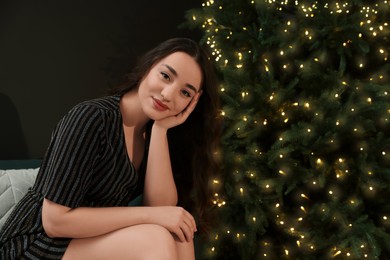 Photo of Beautiful woman near Christmas tree with golden lights indoors