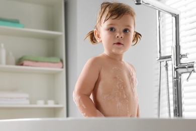 Photo of Cute little girl covered with foam in bathroom