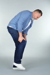 Man suffering from knee pain on light background