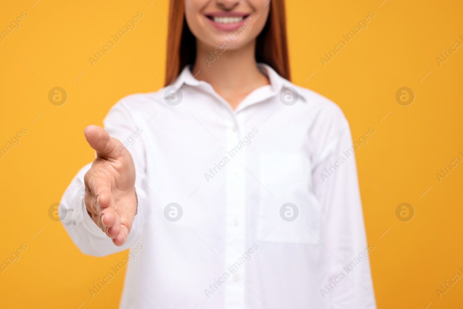 Photo of Woman welcoming and offering handshake on orange background, closeup