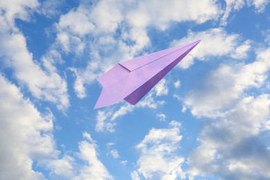 Image of Violet paper plane flying in blue sky with clouds