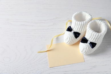Photo of Handmade baby booties and empty greeting card on wooden background. Space for text