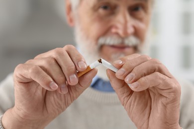 Photo of Stop smoking concept. Senior man breaking cigarette on blurred background, selective focus