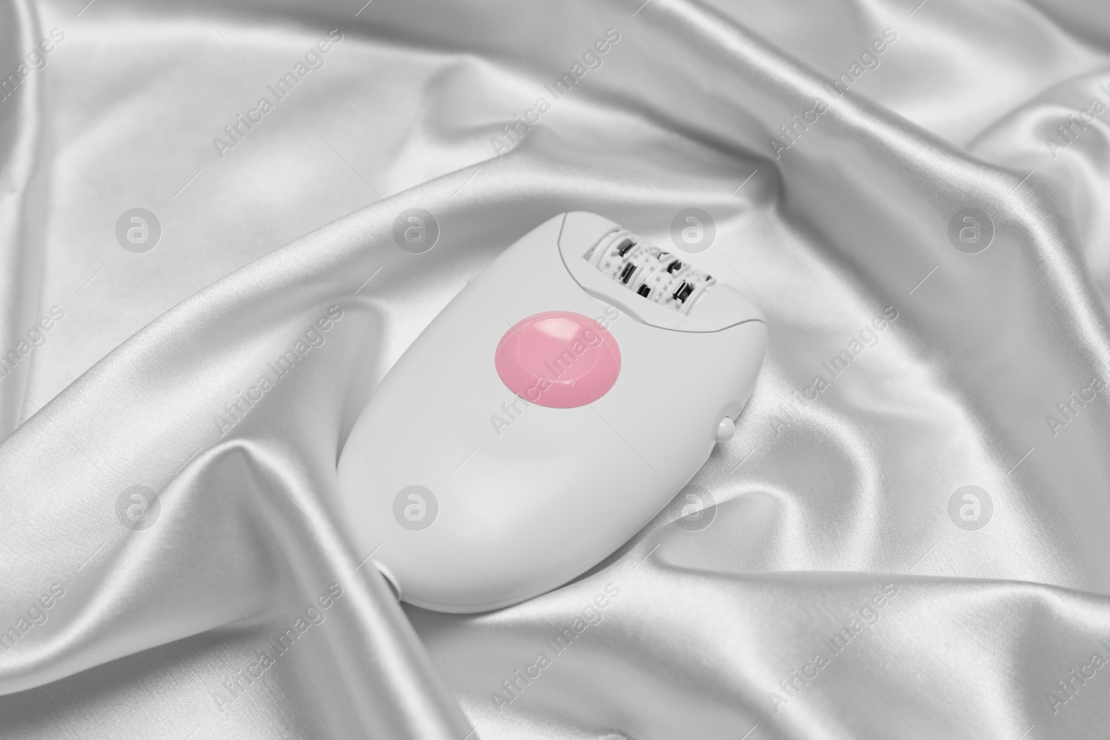 Photo of Modern epilator on white silk fabric. Hair removal