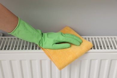Photo of Woman cleaning radiator with rag indoors, closeup