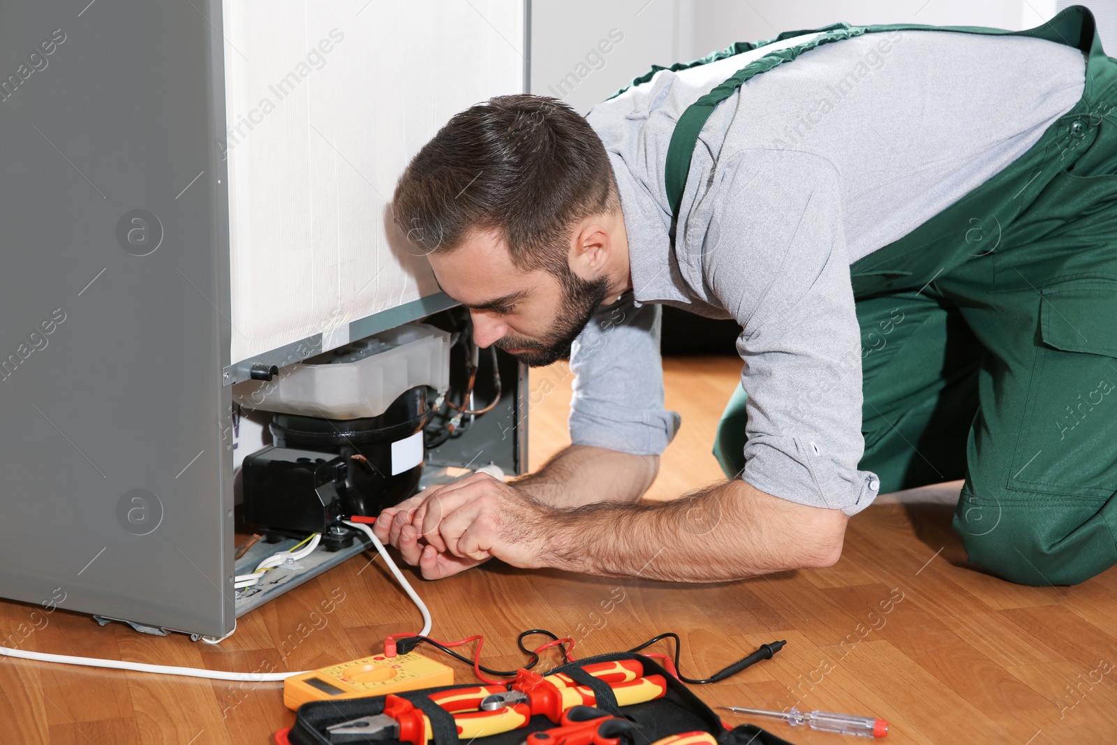 Photo of Male technician in uniform repairing refrigerator indoors