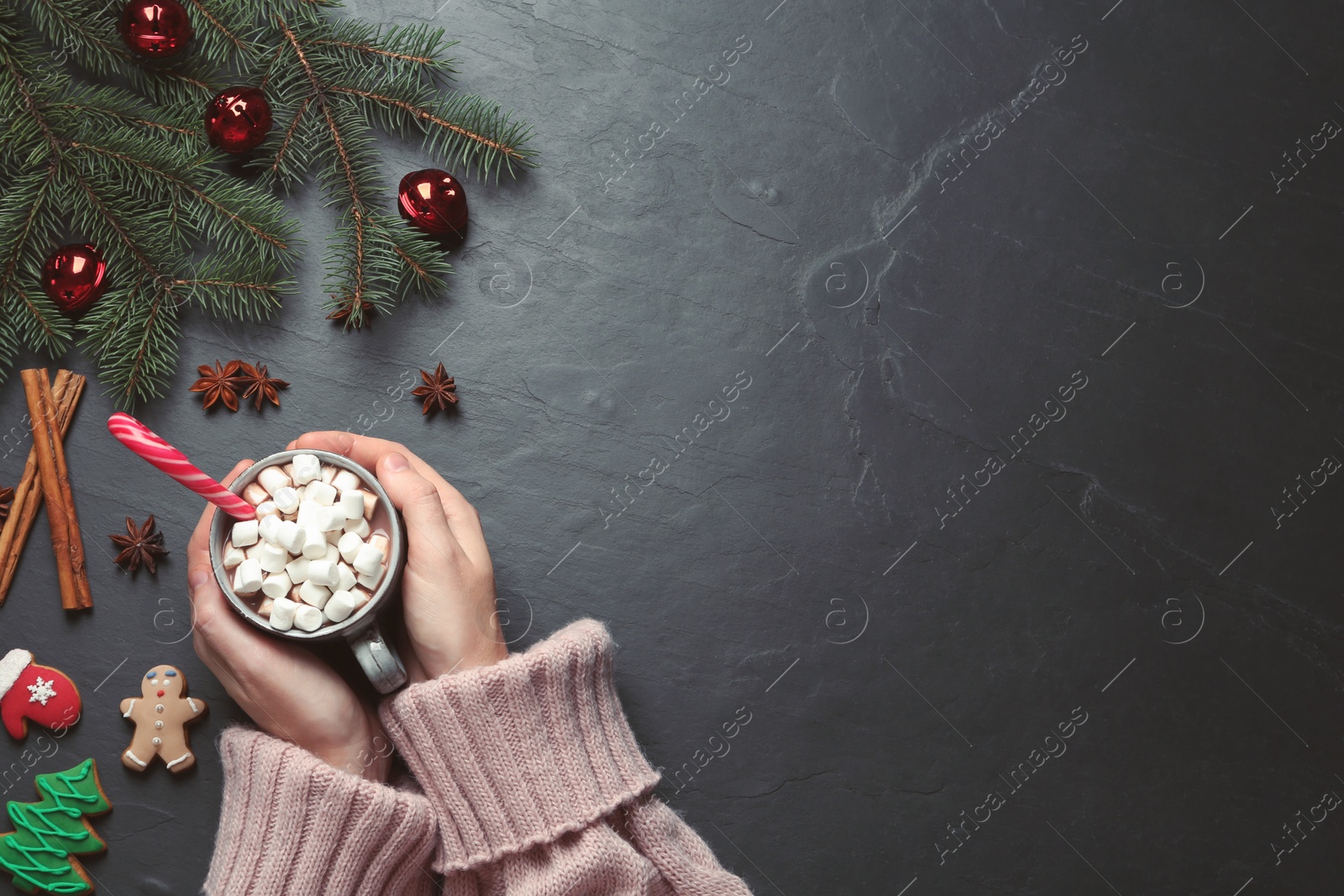 Photo of Woman holding cup of delicious hot chocolate with marshmallows and candy cane at black table, top view. Space for text