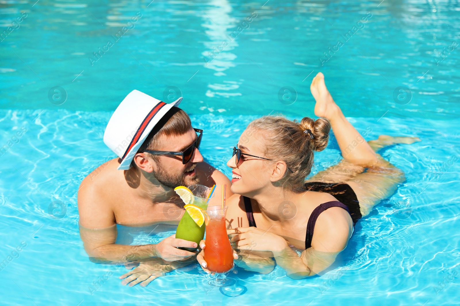 Photo of Young couple with refreshing cocktails in swimming pool at resort