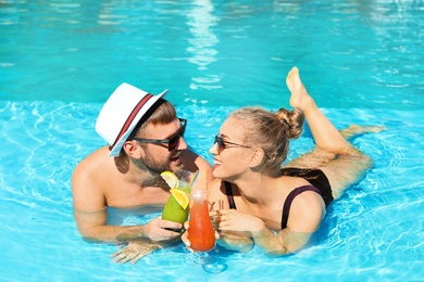 Young couple with refreshing cocktails in swimming pool at resort