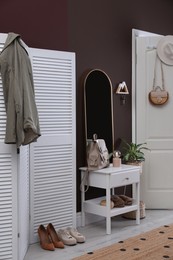 Modern hallway interior with stylish white furniture and wooden hanger for keys on brown wall