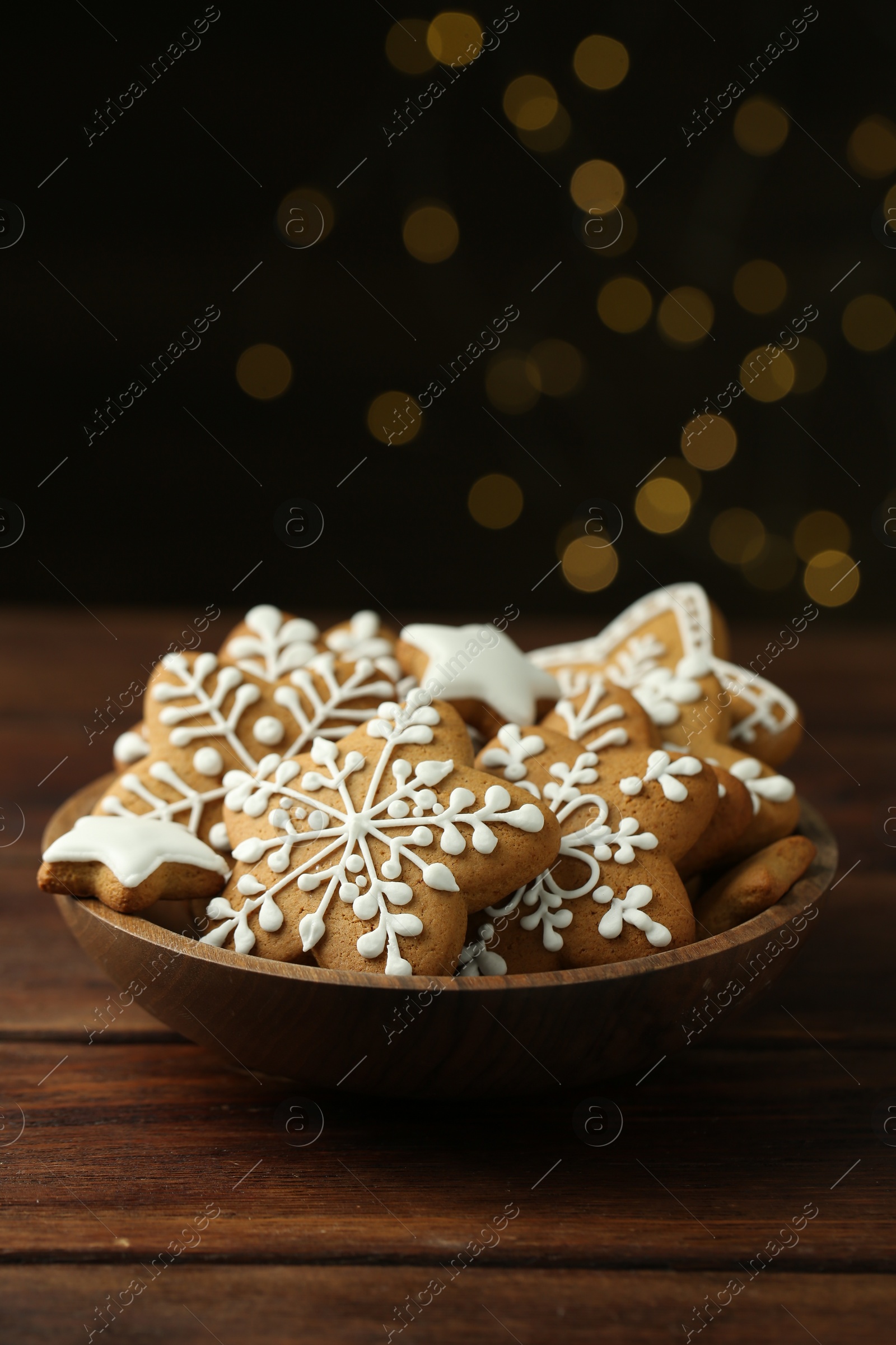 Photo of Tasty Christmas cookies with icing in bowl on wooden table against blurred lights