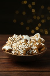 Photo of Tasty Christmas cookies with icing in bowl on wooden table against blurred lights