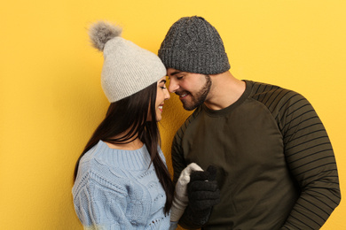 Photo of Happy young couple in warm clothes on yellow background. Winter vacation